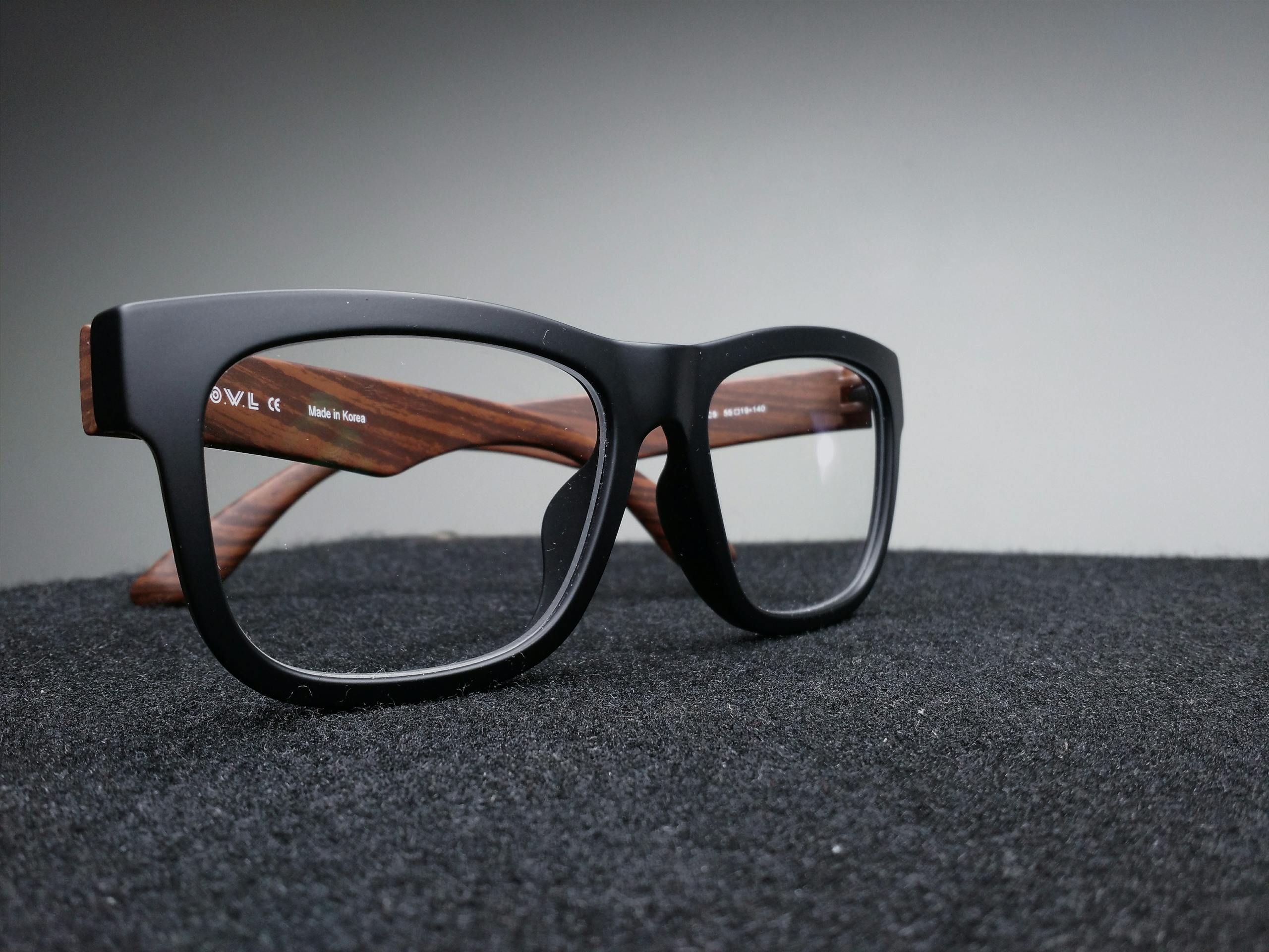 Close-up of fashionable black and wooden frame glasses on dark fabric with a soft-focus background.